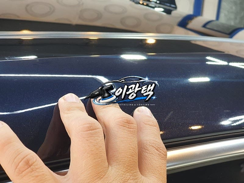 손가락과 함께 근접 촬영한 광이 나는 남색 차량 도장면